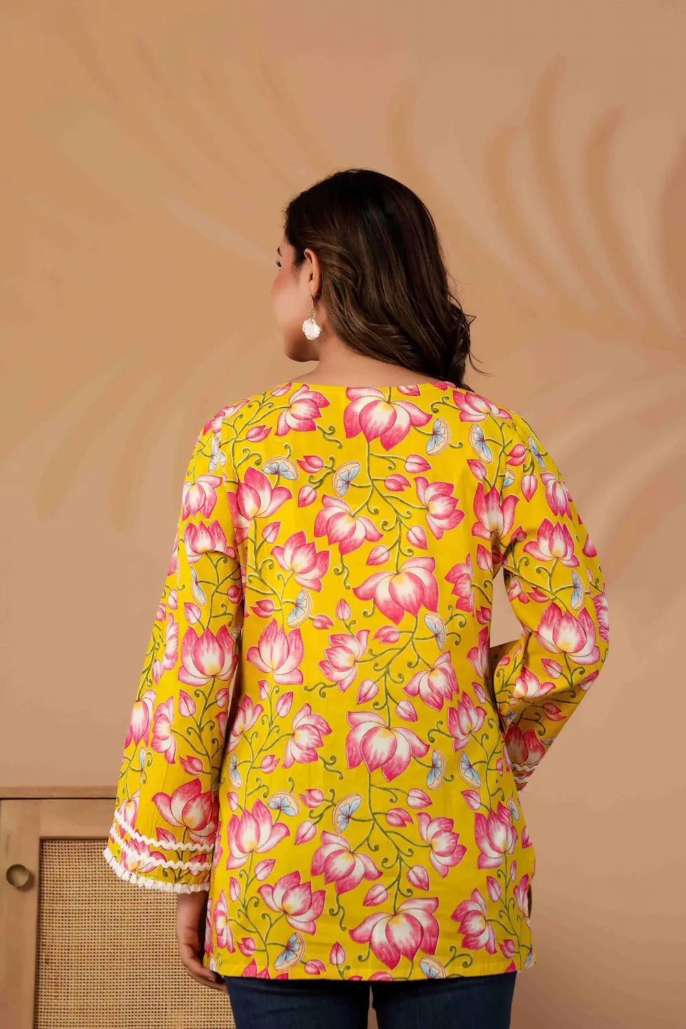 Woman wearing a yellow floral top against a beige background