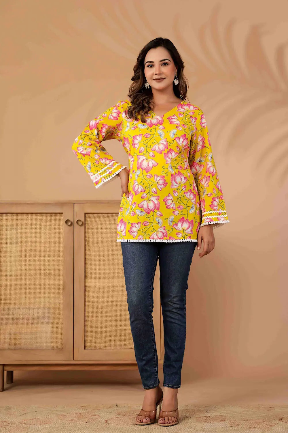 Woman wearing a yellow floral blouse with bell sleeves against a beige background
