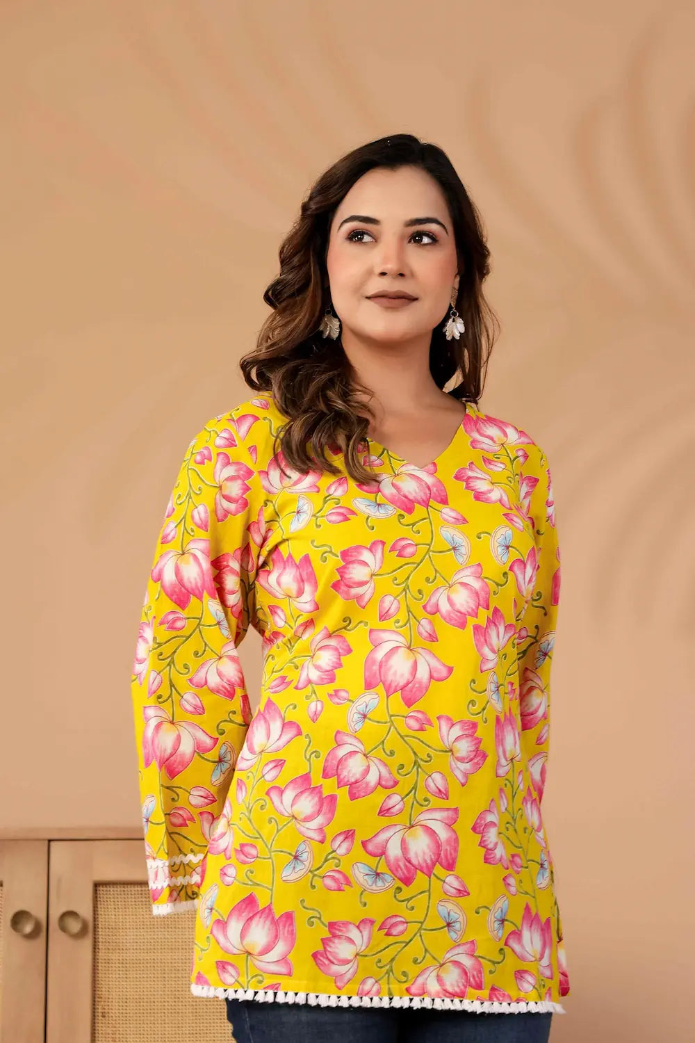 Woman wearing a yellow floral long-sleeve top against a beige background