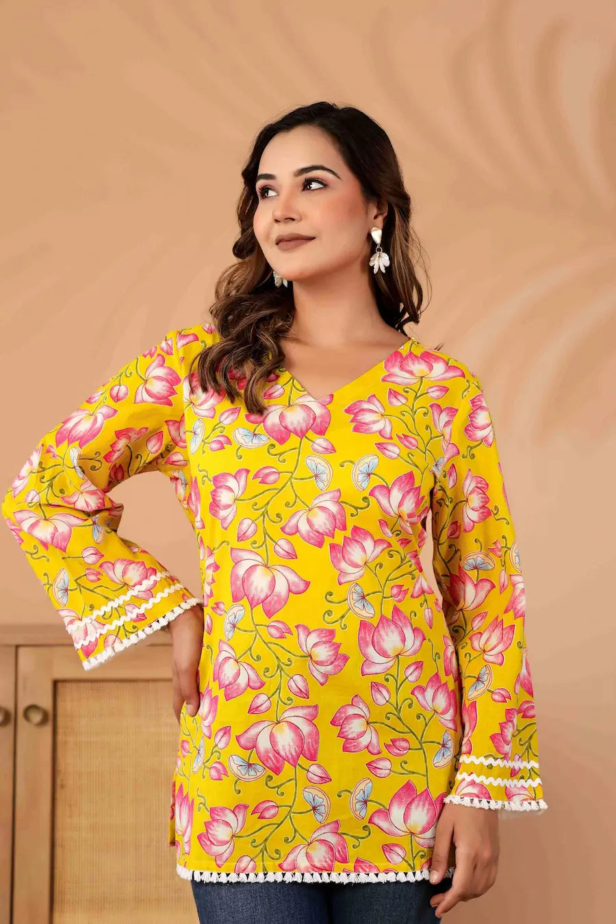 Woman wearing a yellow floral blouse with bell sleeves against a beige background