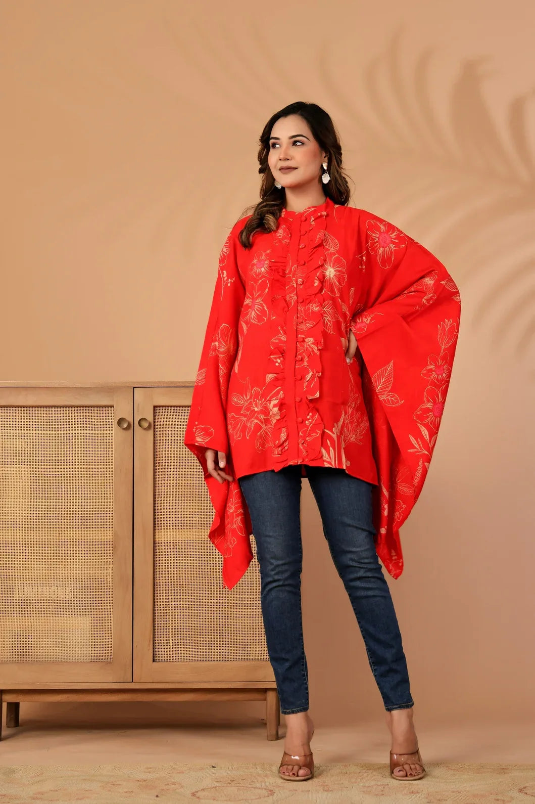 Woman wearing a red floral top and blue jeans against a beige background