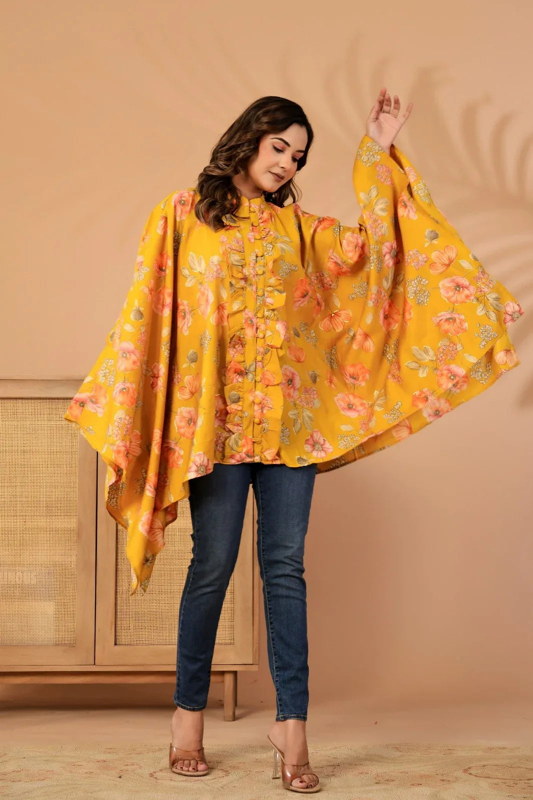 Woman wearing a yellow floral cape over a blue outfit against a beige background-YAVASTRAH