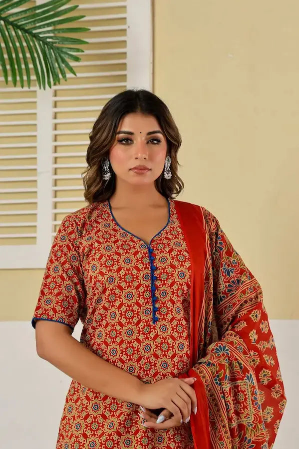 Woman wearing a traditional outfit with a red and orange patterned dress against a neutral background