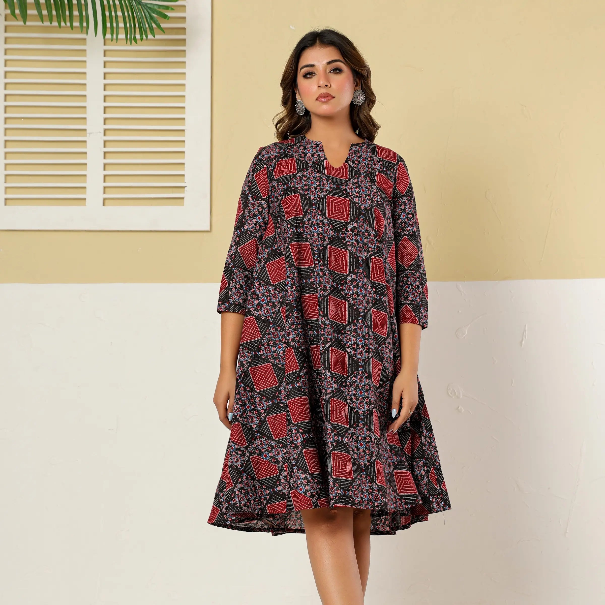 Woman wearing a patterned dress against a beige wall.