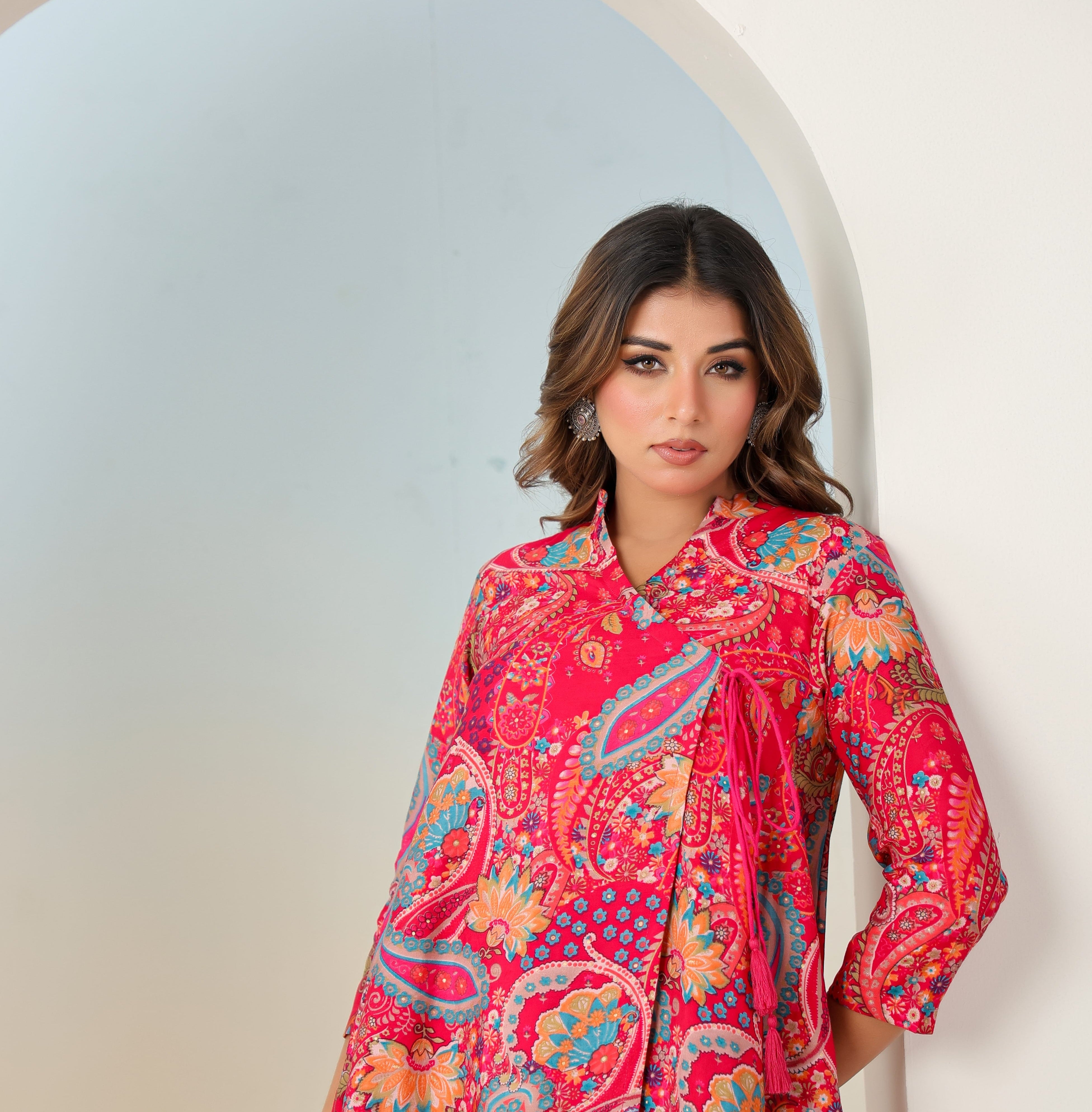 Woman wearing a vibrant red patterned dress standing in front of a white archway.