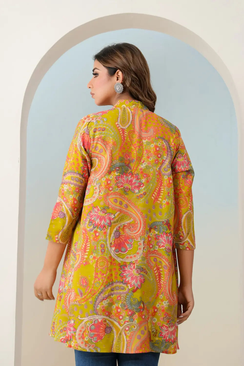 Woman wearing a colorful paisley patterned shirt standing in front of an archway.