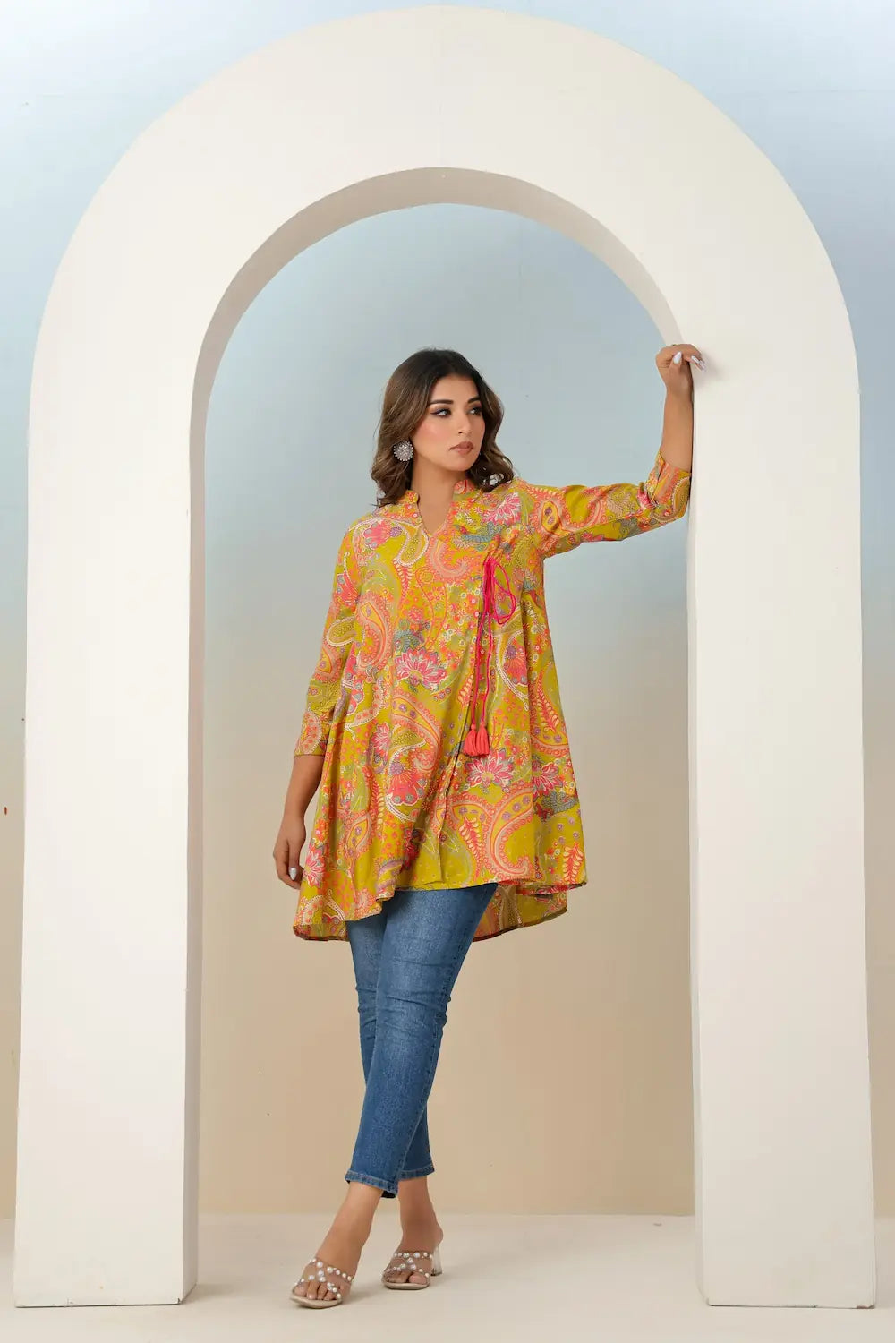 Woman wearing a colorful floral dress standing in front of a white archway.