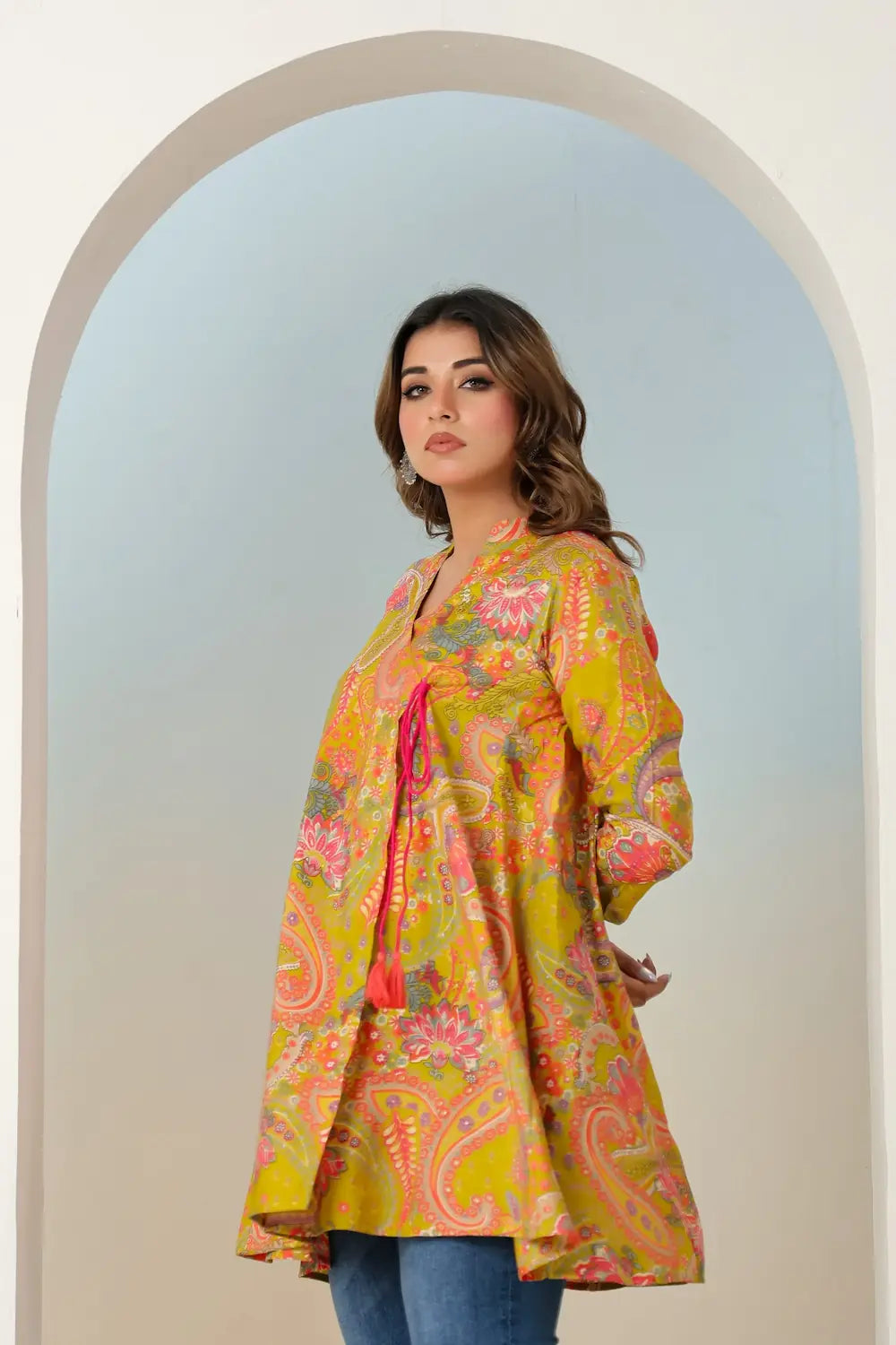 Woman wearing a colorful floral kimono-style jacket standing in front of an archway.