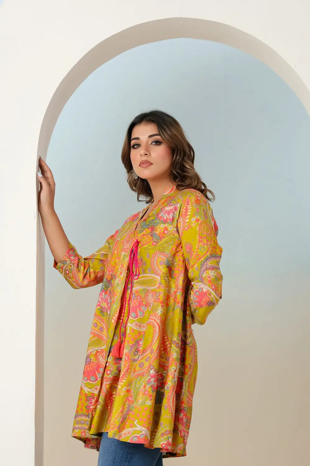 Woman wearing a colorful patterned top standing in front of an archway.