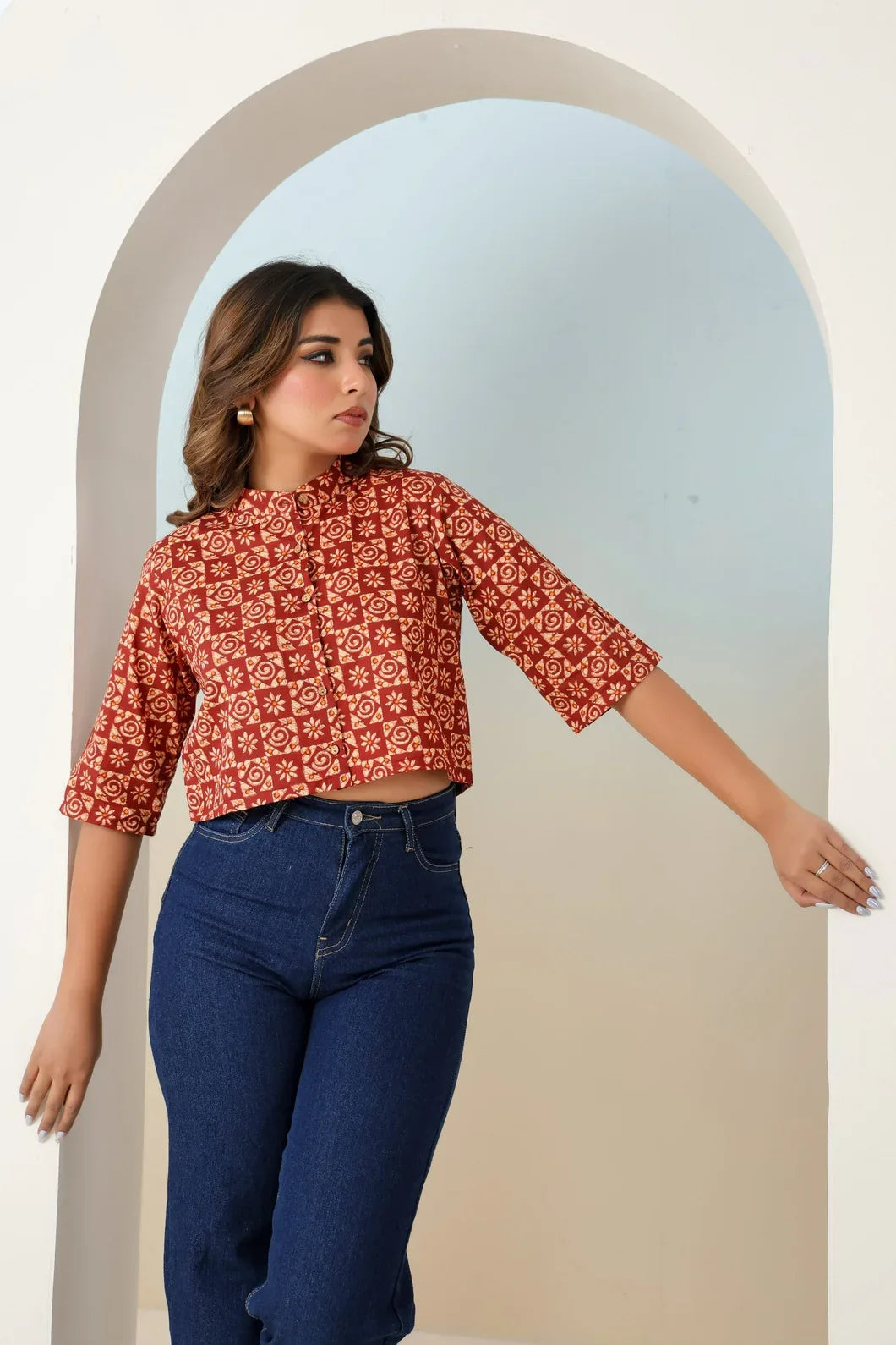 Woman wearing a red floral blouse and blue jeans standing in front of an archway.