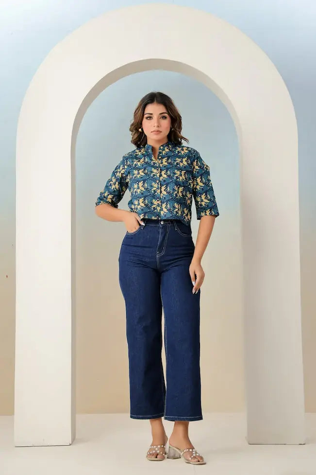 Woman wearing a blue floral blouse and jeans standing under a white archway.