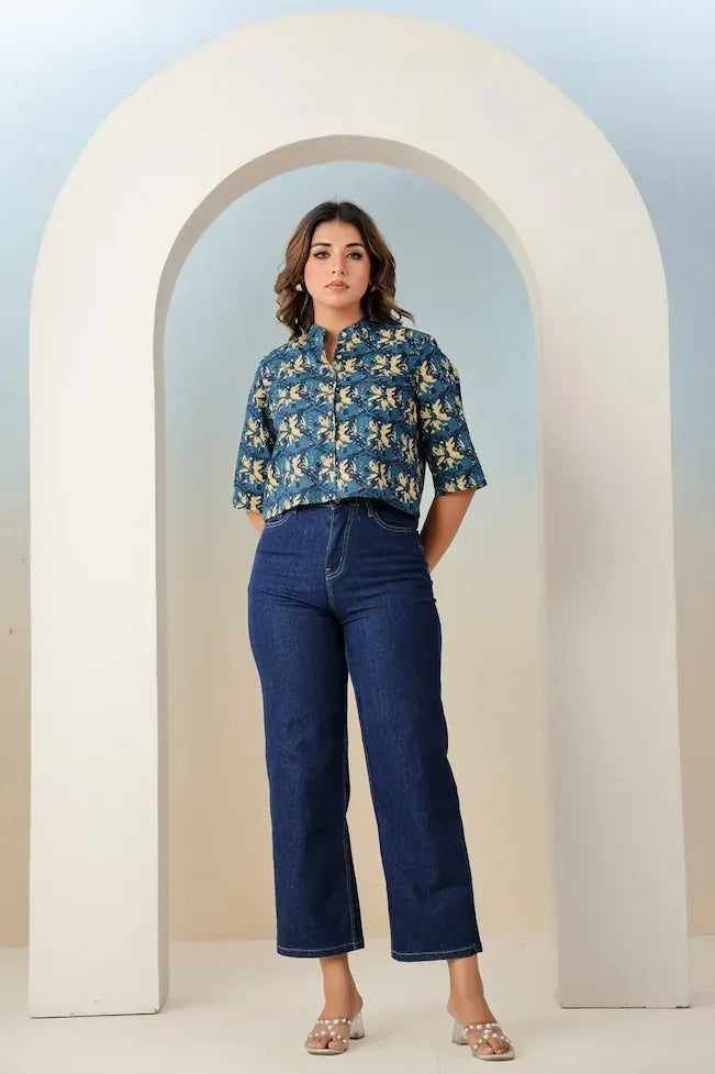 Woman wearing a blue floral blouse and jeans standing in front of a white archway.