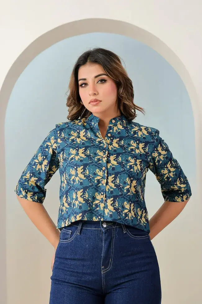 Woman wearing a blue floral blouse and jeans standing in front of an archway.