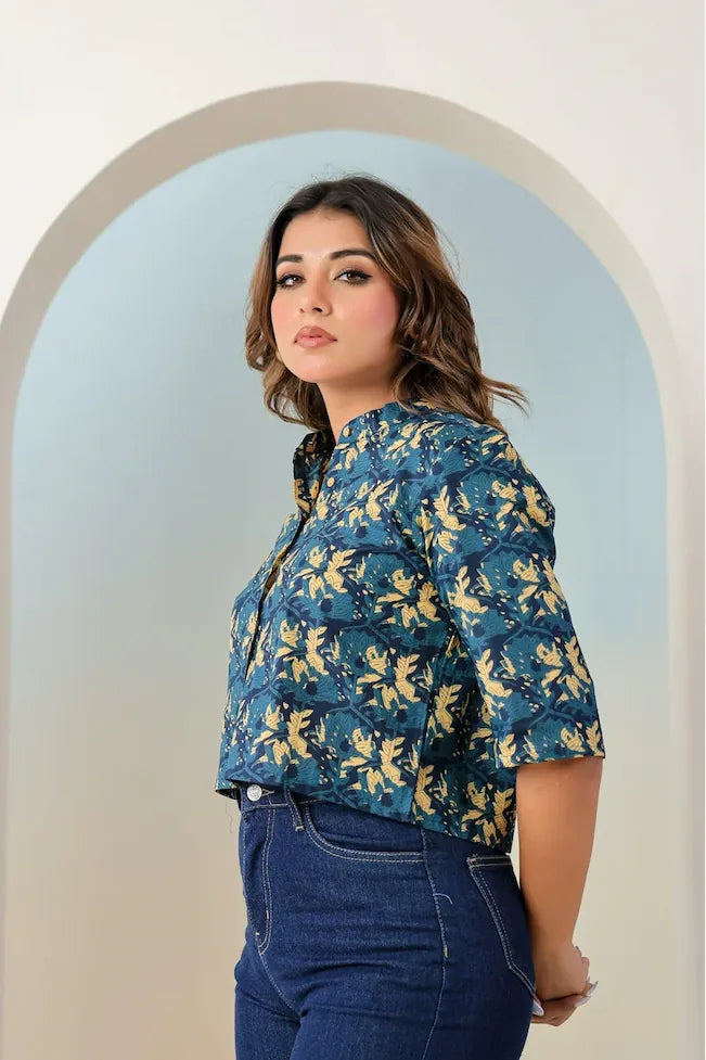 Woman wearing a blue floral blouse and jeans standing in front of an archway.