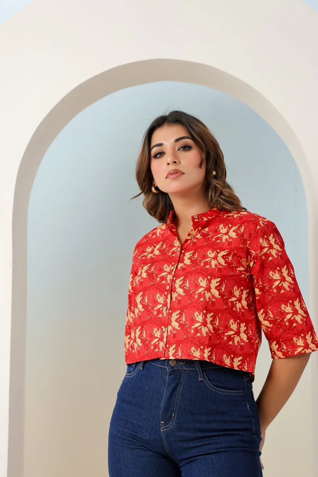 Woman wearing a red floral crop top standing in an archway - YAVASTRAH