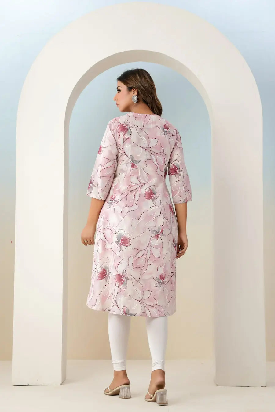 Woman wearing a pink floral dress standing in front of a white archway.