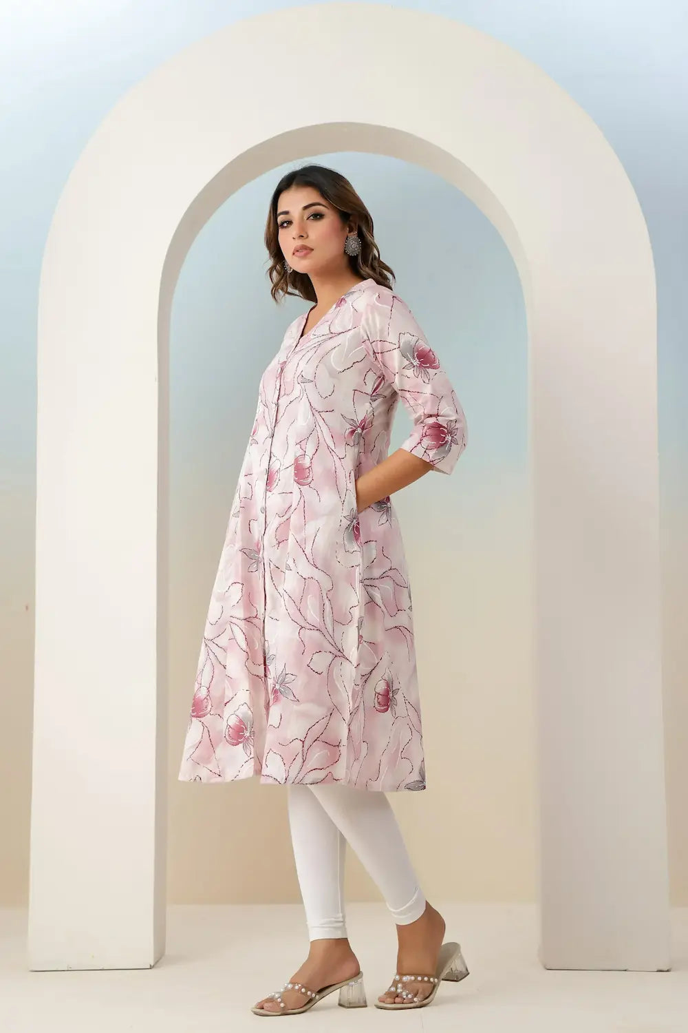 Woman wearing a pink floral dress standing in front of a white archway.