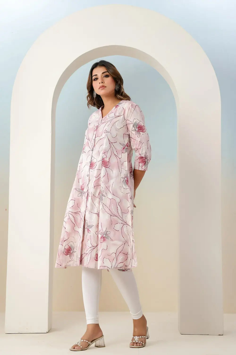 Woman wearing a pink floral dress standing in front of a white archway.