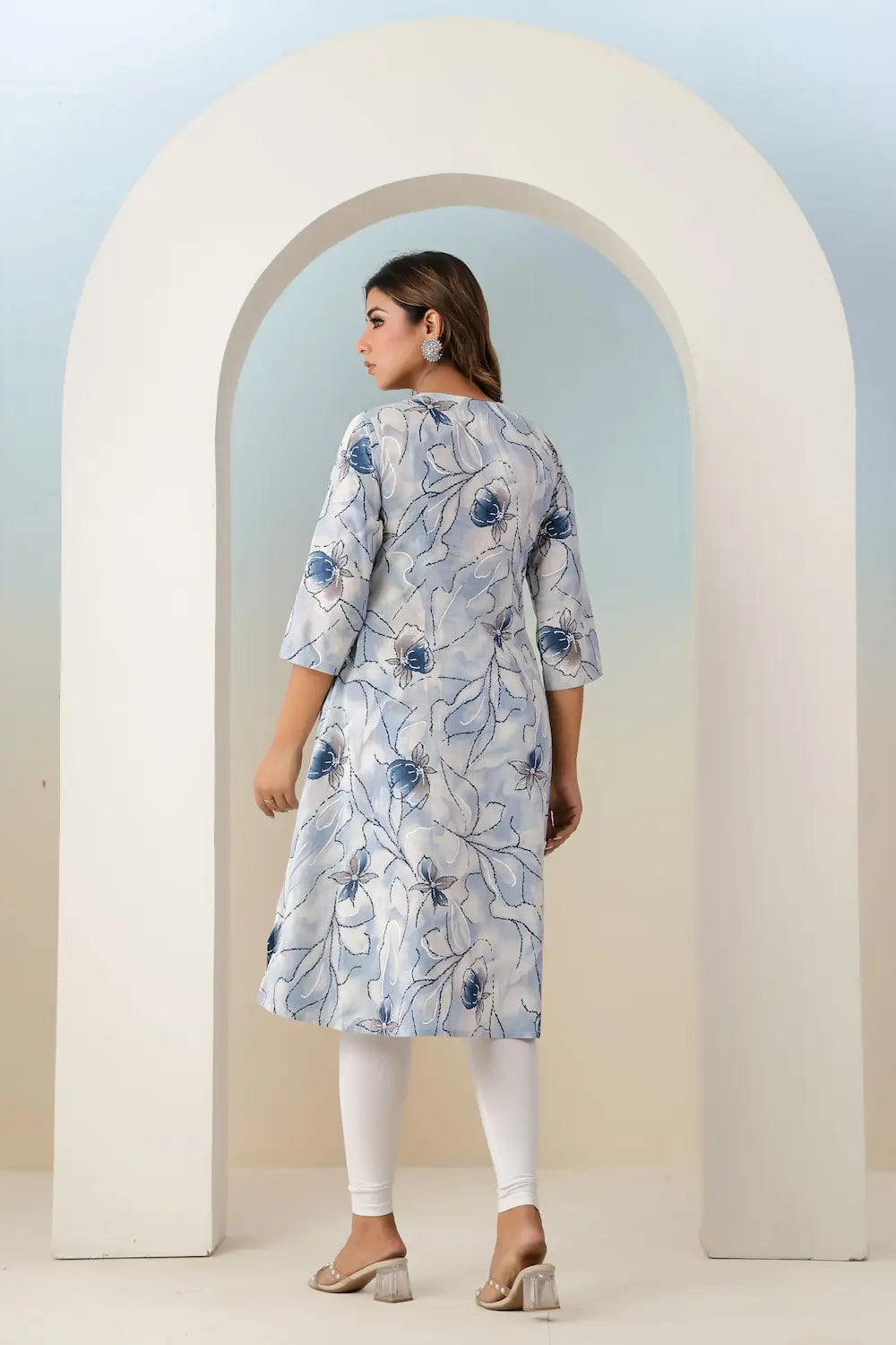 Woman wearing a floral dress standing in front of a white archway.