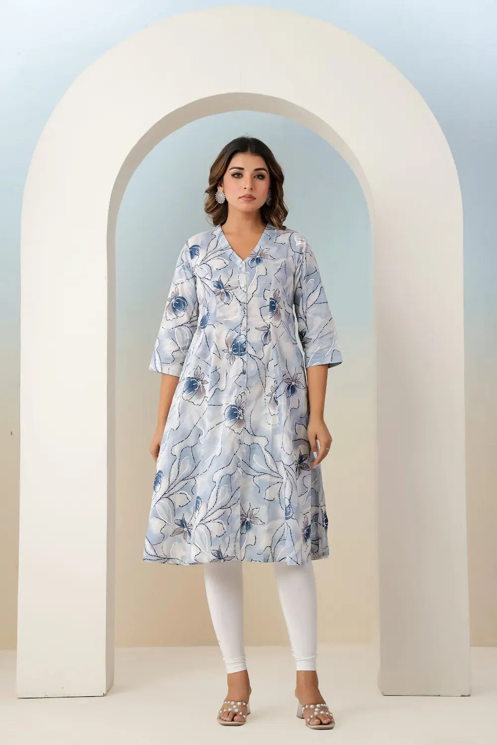 Woman wearing a blue floral dress standing in front of a white archway.