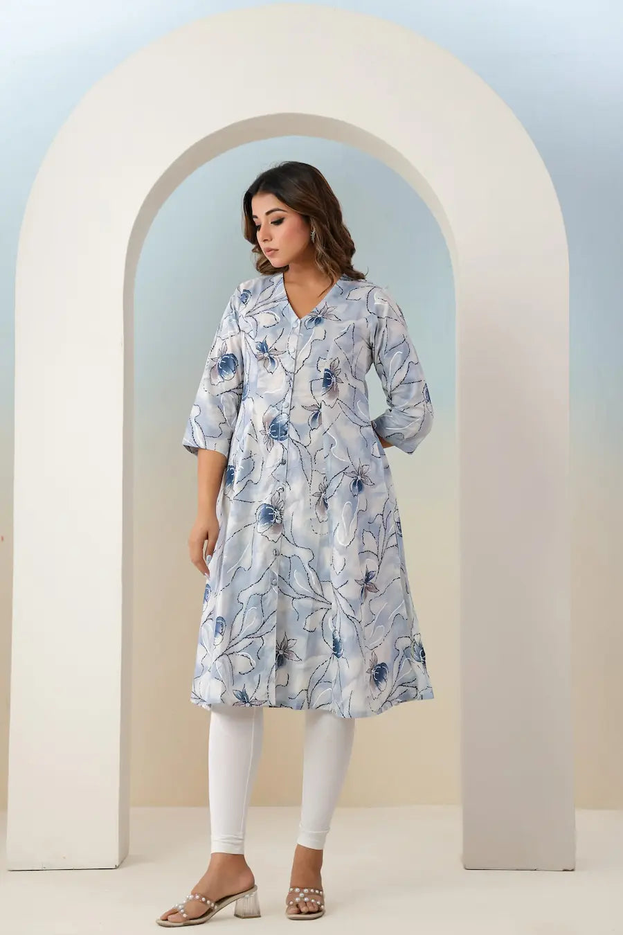 Woman wearing a floral dress standing in front of an archway with a light blue background