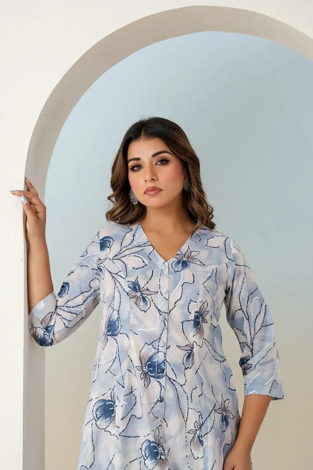 Woman wearing a blue floral dress standing against a light blue wall.