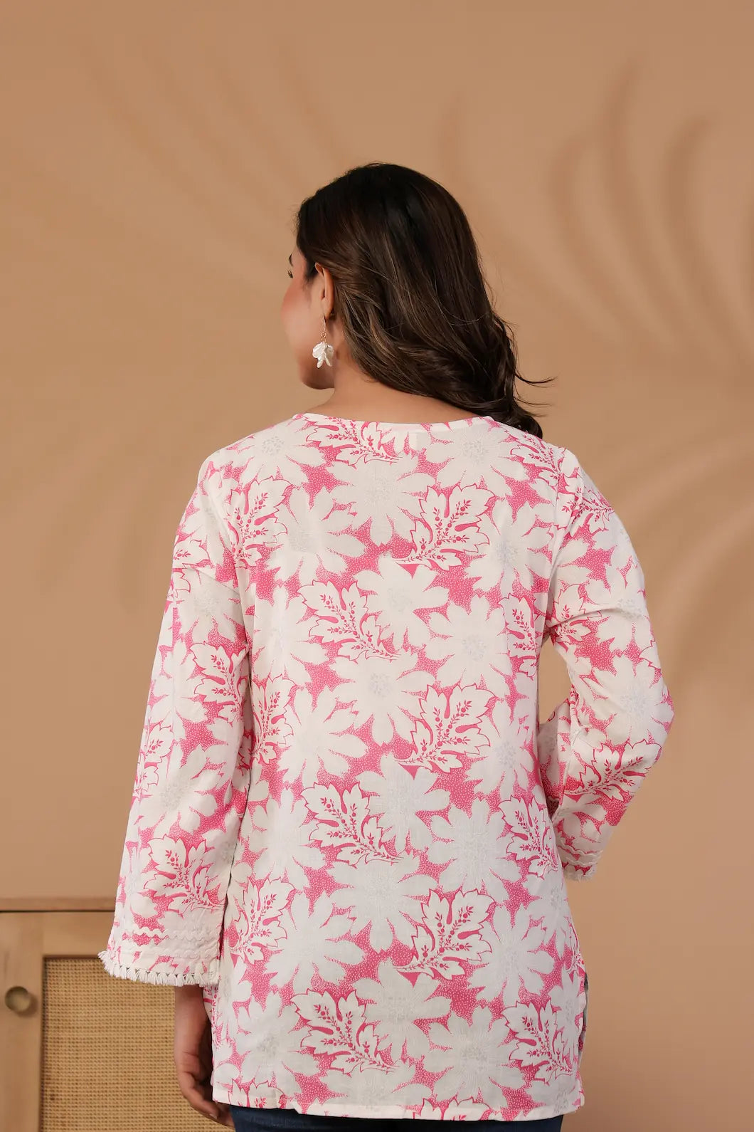 Woman wearing a pink and white floral patterned top against a beige background