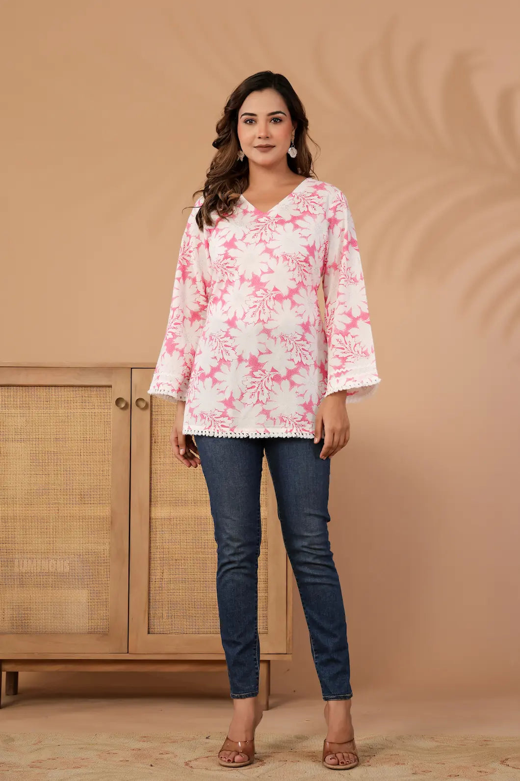 Woman wearing a pink floral blouse and blue jeans against a beige background