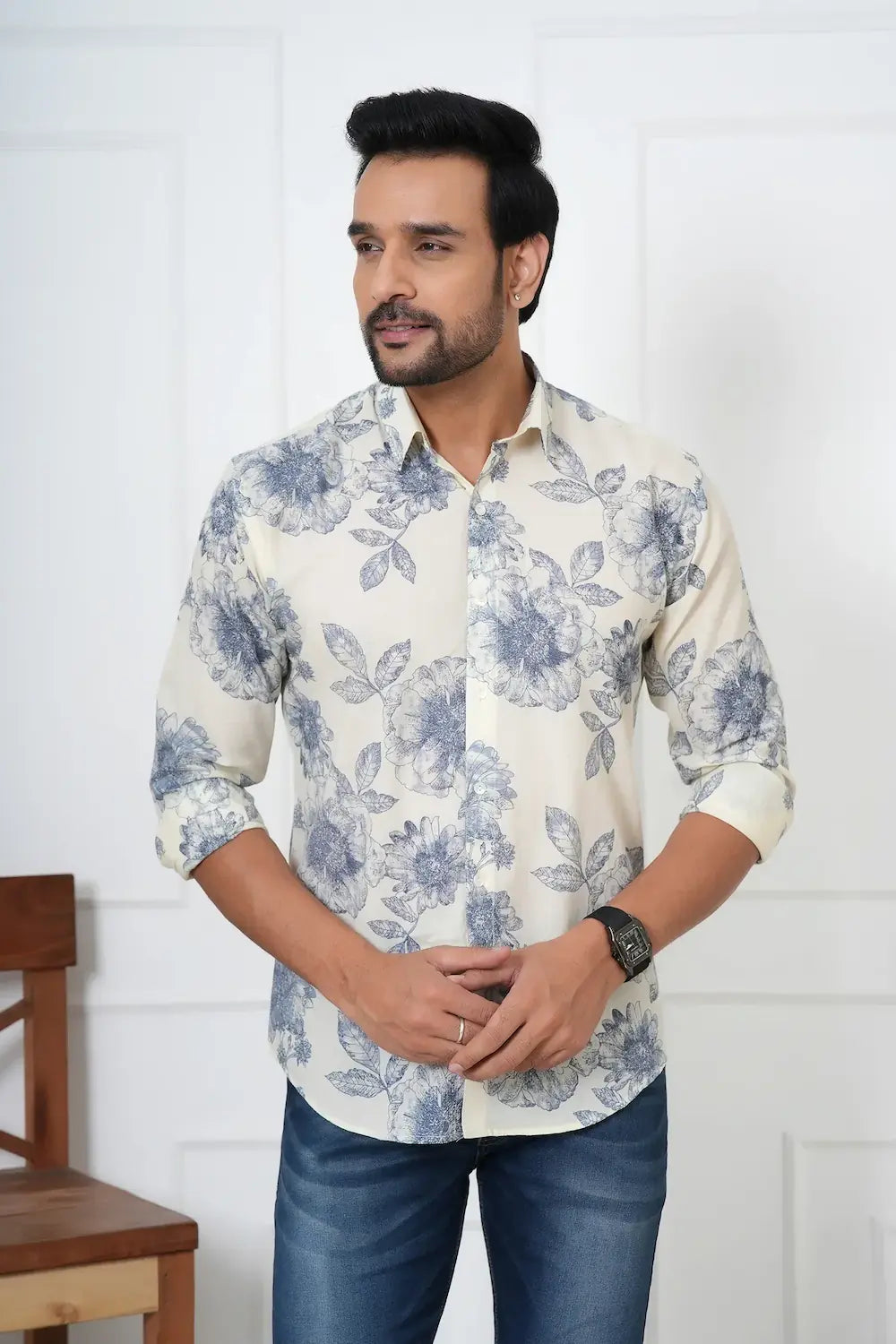 Man wearing a white shirt with blue floral pattern and blue jeans indoors.