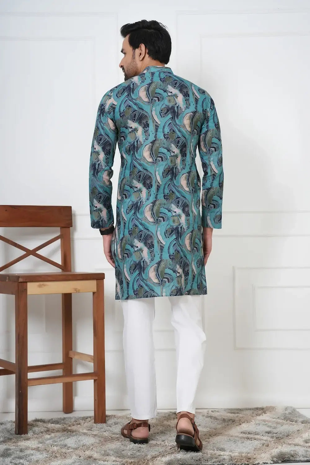 Man wearing a patterned kurta with white pants in a minimalistic setting.