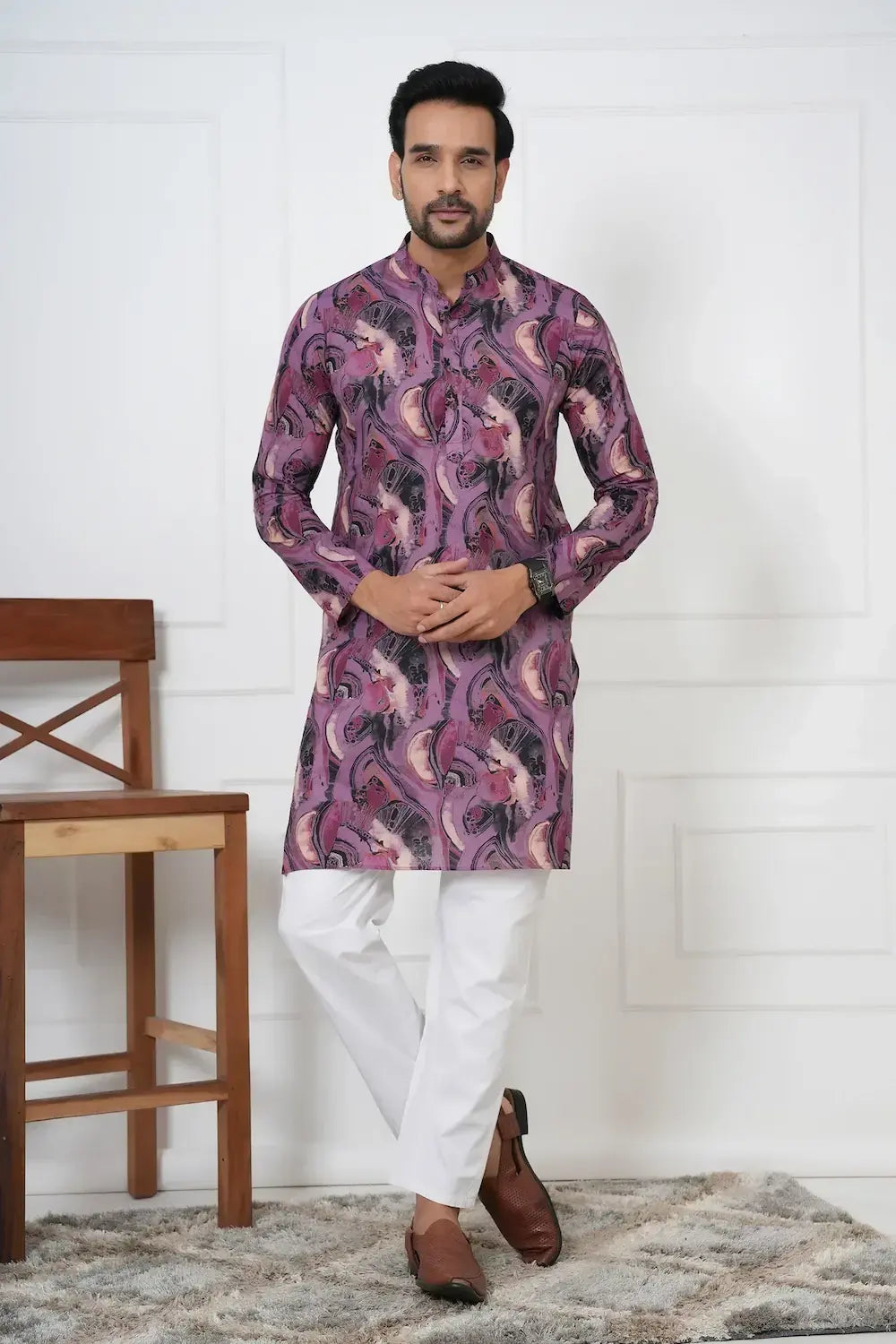 Man wearing a patterned kurta with white pants in a room with a wooden chair and white wall.
