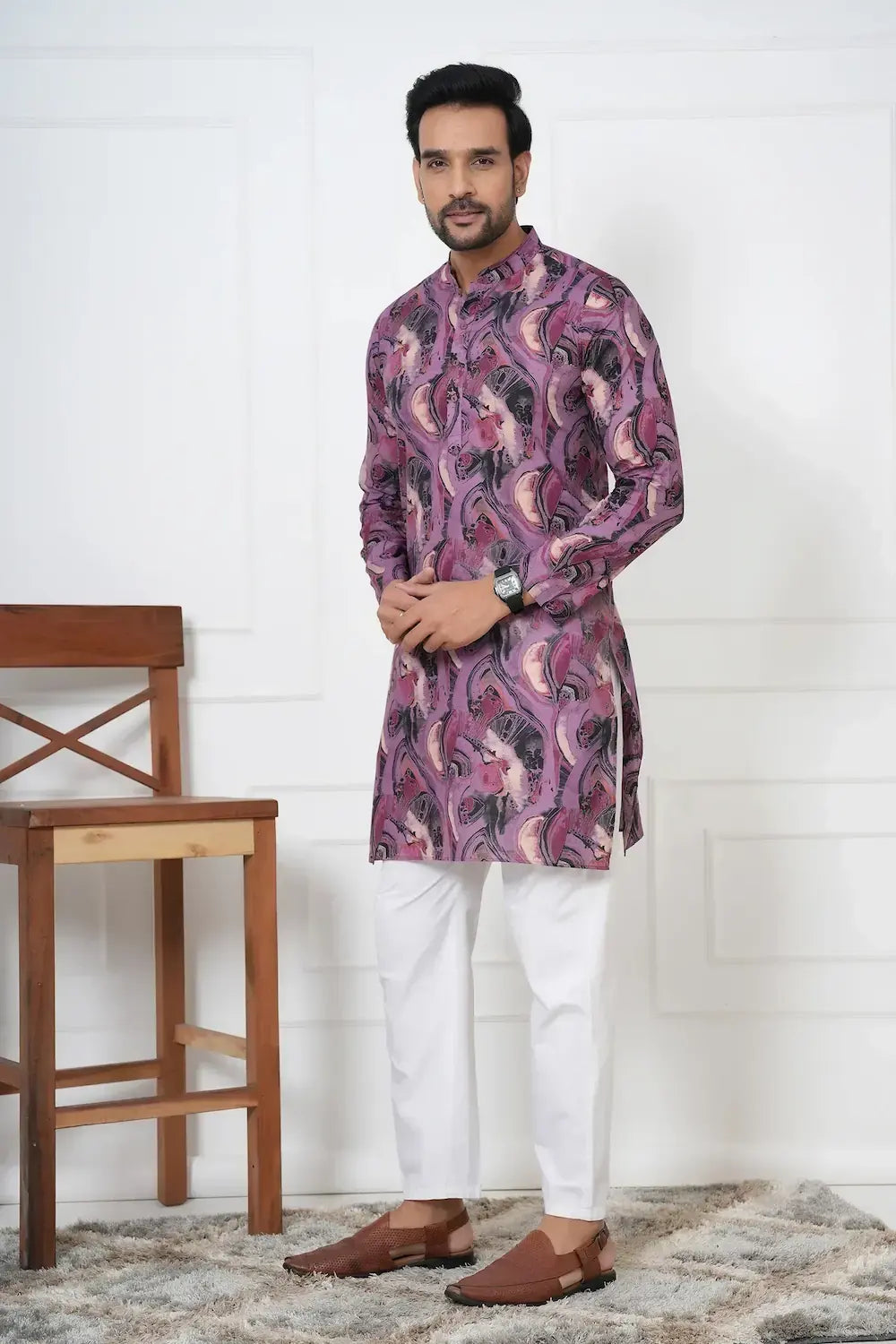 Man wearing a patterned kurta with white pants in a room with wooden furniture.