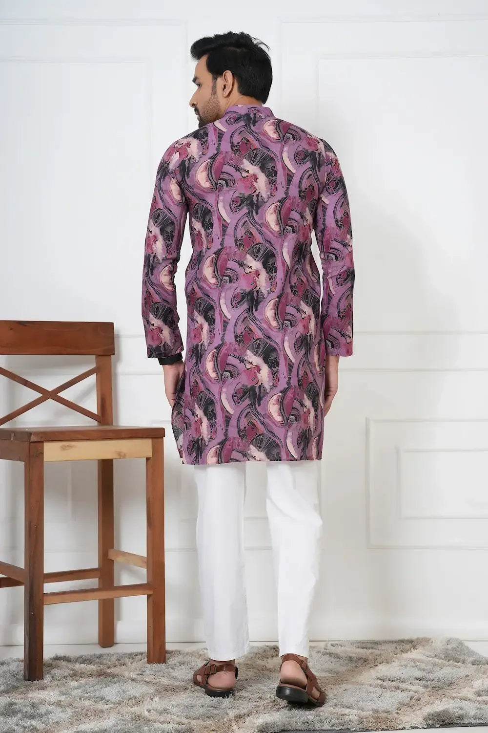 Man wearing a patterned kurta with white pants in a minimalistic setting.